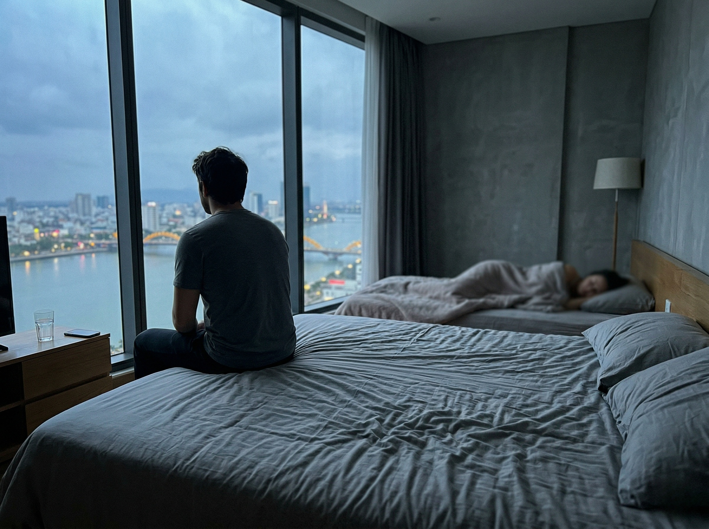 person-sitting-on-edge-of-bed-looking-at-cityscape